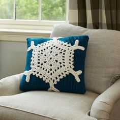 a white crocheted pillow sitting on top of a chair next to a window