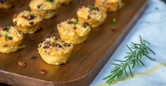 mini muffins with meat and cheese on a wooden tray next to a sprig of rosemary