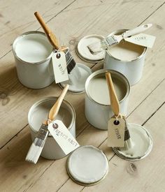 several paint cans with brushes in them on a wooden floor next to two empty white buckets