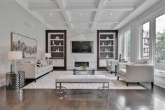 a large living room with white furniture and wood flooring, along with high ceilings