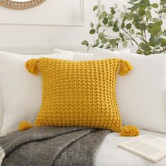 an orange knitted pillow sitting on top of a white couch next to a book