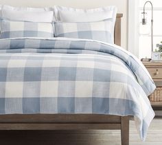 a blue and white checkered comforter set on a bed with two pillows in the background