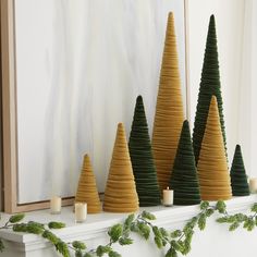 christmas trees are lined up on the mantle in front of a painting and candle holders