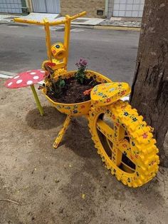 a yellow wheel barrow with flowers in it next to a tree