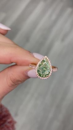 a woman's hand holding an engagement ring with a green stone