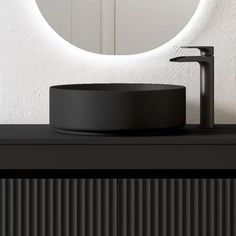 a round mirror on the wall above a black counter top with a faucet