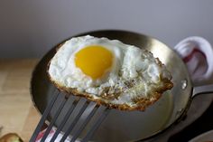 an egg is being cooked in a frying pan with a fork on the side