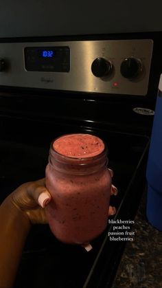 a hand holding a jar of smoothie in front of an oven