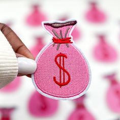 a hand holding a small pink bag with the letter s in it and red thread