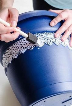 a person is painting a blue bucket with white lace on the rim and holding a brush