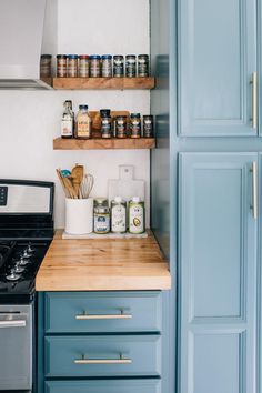 a kitchen with blue cabinets and wooden shelves above the stove top is filled with spices