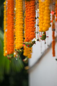 orange and yellow garlands hanging from the ceiling in front of a white wall with greenery