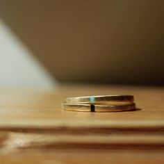 two gold wedding bands sitting on top of a wooden table