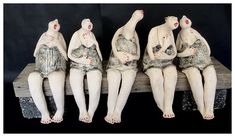 four ceramic figures sitting on top of a wooden bench with their legs spread out and hands in the air