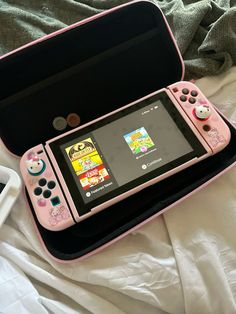 a pink nintendo wii game system sitting on top of a white bed next to a black case