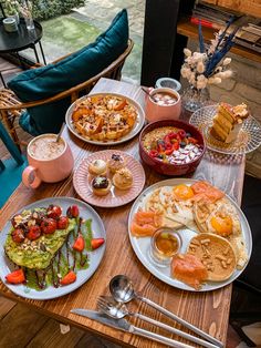 a wooden table topped with lots of plates of food next to cups and spoons