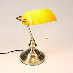 a yellow table lamp on a white surface with a cord plugged into the base