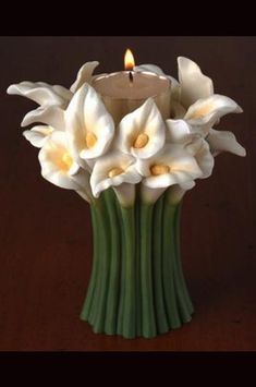 white flowers in a green vase with a lit candle on the top and dark background