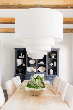 a dining room table with white chairs and a large light fixture hanging over it's head