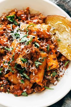 a white bowl filled with pasta and meat covered in parmesan cheese on top