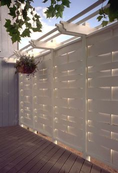 a white fence with plants hanging from it's sides and lights on the side