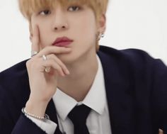 a man with blonde hair wearing a suit and tie sitting at a table in front of a white background