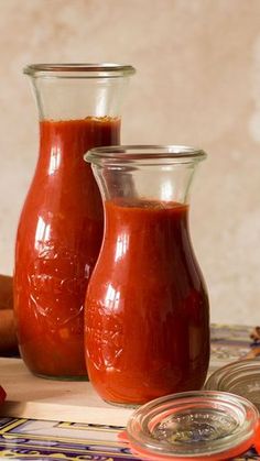 two glass vases filled with red sauce sitting on top of a table