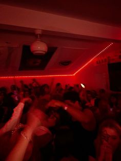 a group of people standing in a room with red lights on the ceiling and one person holding up his cell phone