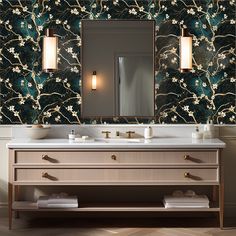 a bathroom vanity with two sinks and a large mirror above it, in front of a floral wallpaper