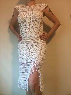 a woman wearing a white crochet dress and heels standing in front of a wall