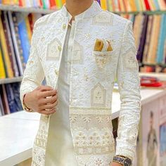 a man standing in front of a bookshelf wearing a white suit