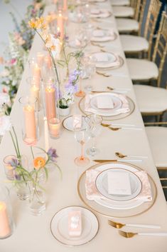 a long table is set with white plates and gold place settings for dinner guests to enjoy