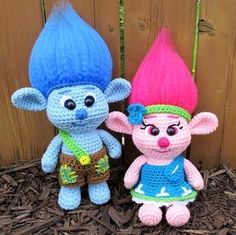 two crocheted stuffed toys sitting next to each other on the ground in front of a fence