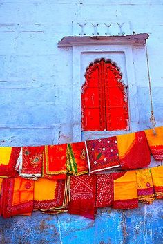 an orange and yellow cloth hanging from a blue wall with a red window in the background