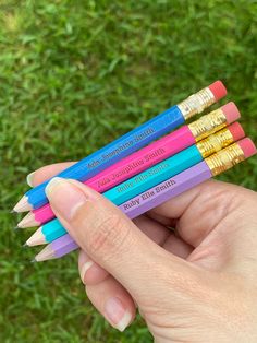 a person holding four colored pencils in their left hand on the green grass outside