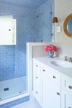 a blue and white bathroom with flowers in a vase on the sink counter next to the shower