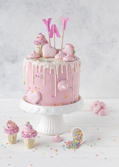 a pink cake with sprinkles and cupcakes on the top is surrounded by confetti