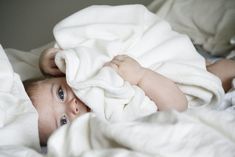 a baby laying in bed under a white blanket