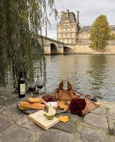 a picnic on the bank of a river with bread, cheese and wine in front of it