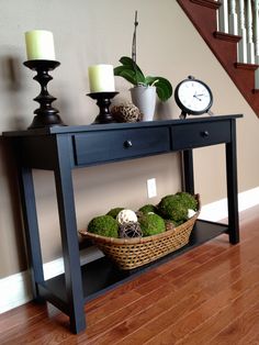 a wooden table topped with green plants next to a clock and candle holders on top of a hard wood floor