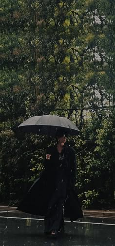 a woman walking in the rain with an umbrella over her head and black coat on