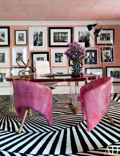 a living room with pink chairs and pictures on the wall behind them in black and white stripes