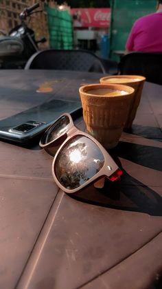 a pair of sunglasses sitting on top of a table next to a cup and cell phone