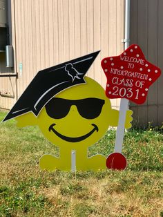 a sign with a graduate hat and sunglasses on it in the grass next to a building