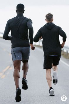 two men are running down the road in shorts and sweatshirts with their backs turned to the camera