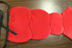 four pieces of red cloth with black straps on a wooden table next to a pair of scissors