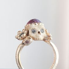 A garden snake wraps around a skull resting in a bed of flowers in an allegory come to life that you can wear on your finger. Named Nozarashi, Japanese for "weather beaten bones" in a twist on traditional memento mori rings. A snake for shedding old ways, flowers for growth, and an open minded skull to live life to the fullest. One of a kind and handmade in solid 14k yellow gold by Nick Potash in his Maui, Hawaii Studio. Carved 1.86ct pink tourmaline brain (there is a small imperfection in the back, but aren't all brains a little imperfect?), blue sapphire flowers, salt & pepper diamond skull eyes and a single orange sapphire snake eye. Size 4.5 and not resizable. Each Nozarashi Skull ring comes in a traditional Japanese Paulownia wood box designed to protect heirlooms from the environment Pearl Skull Ring, Skull Eyes, Garden Snake, Wood Box Design, Memento Mori Ring, Bed Of Flowers, Diamond Skull, Paulownia Wood, Old Ways