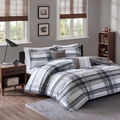 a bed with plaid comforter and pillows on top of it in front of a window