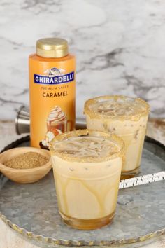 two glasses filled with ice cream sitting on top of a metal tray next to an orange bottle