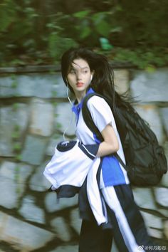 a woman with long black hair is walking down the street while listening to headphones